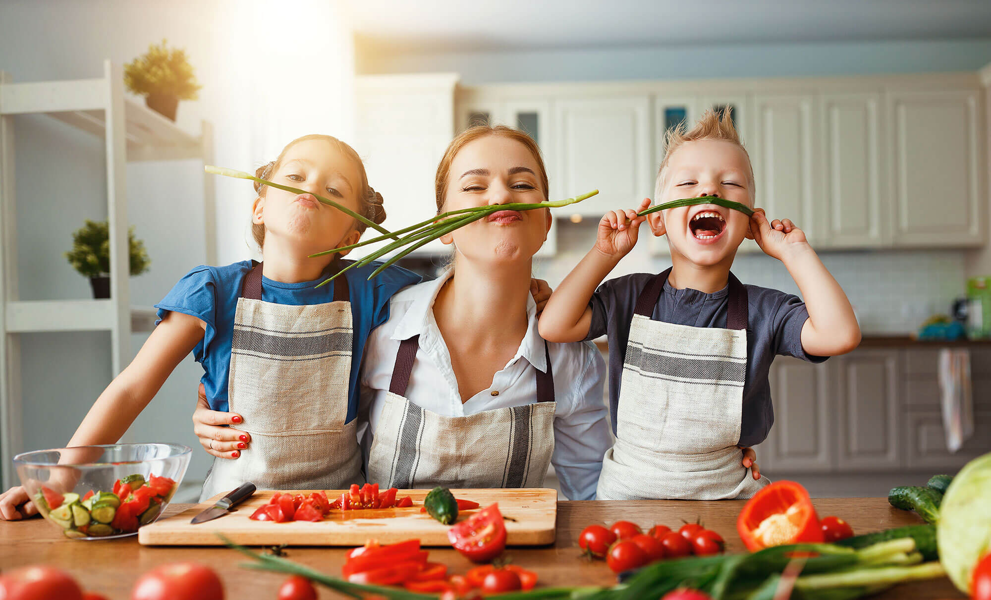 A mother, daughter and son having fun in the kitchen making mustaches with green onion stems
